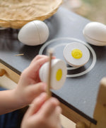 Child holding wooden knife next to a PlanToys egg to cut