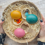 Three PlanToys Eggs in a basket each containing various little treasures. One has beads inside, one has a baby Nin and the third has handwritten little note.