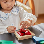 Close up of young girl sat playing with the PlanToys plastic-free wooden fraction blocks set