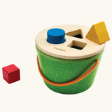 Close-up of a toddler's hand fitting the blue cylinder into the bucket lid