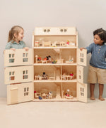 Children playing with the PlanToys Grand Victorian Dollhouse. Door shown open and all floors and attic room has PlanToys dolls house furniture inside.