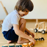 Child playing with PlanToys wooden trains connecting two sets via the magnetic connectors.