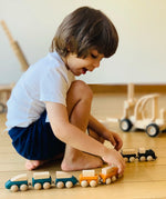 Child playing with PlanToys wooden trains connecting two sets via the magnetic connectors.