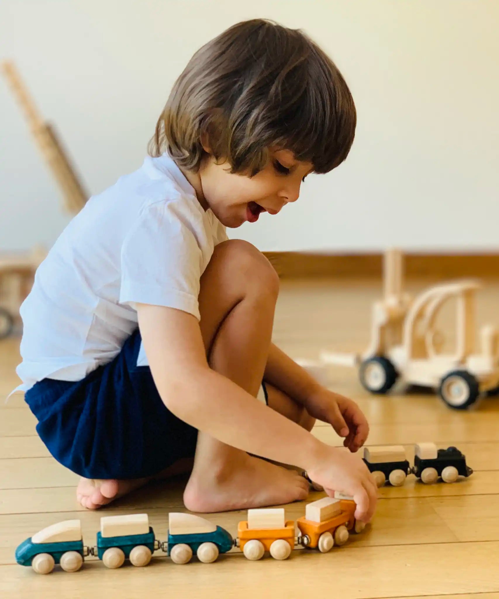 Child playing with PlanToys wooden trains connecting two sets via the magnetic connectors.