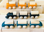 Three PlanToys wooden trains placed on wooden blocks. One yellow, one black and one blue. 