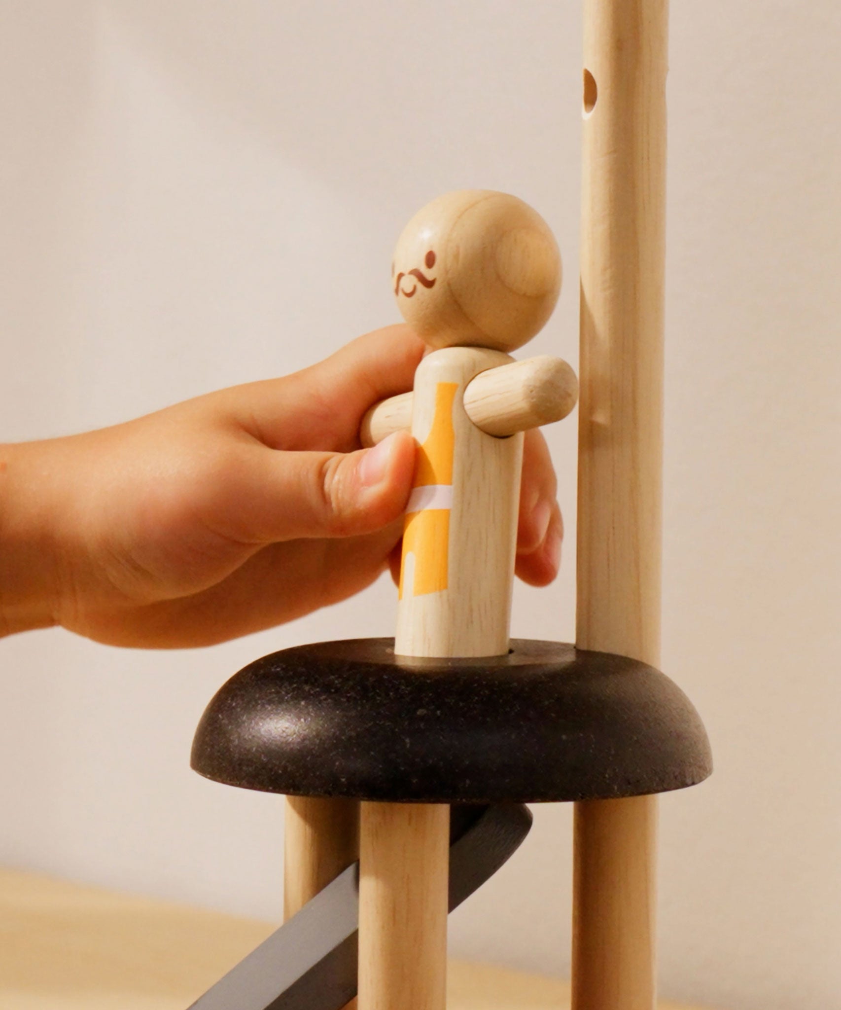 A close up of a child's hand placing the acrobat figure on the PlanToys Natural Rubberwood Jumping Acrobat Toy. PlanToys have a vast range of sustainable wooden toys are available at Babipur.