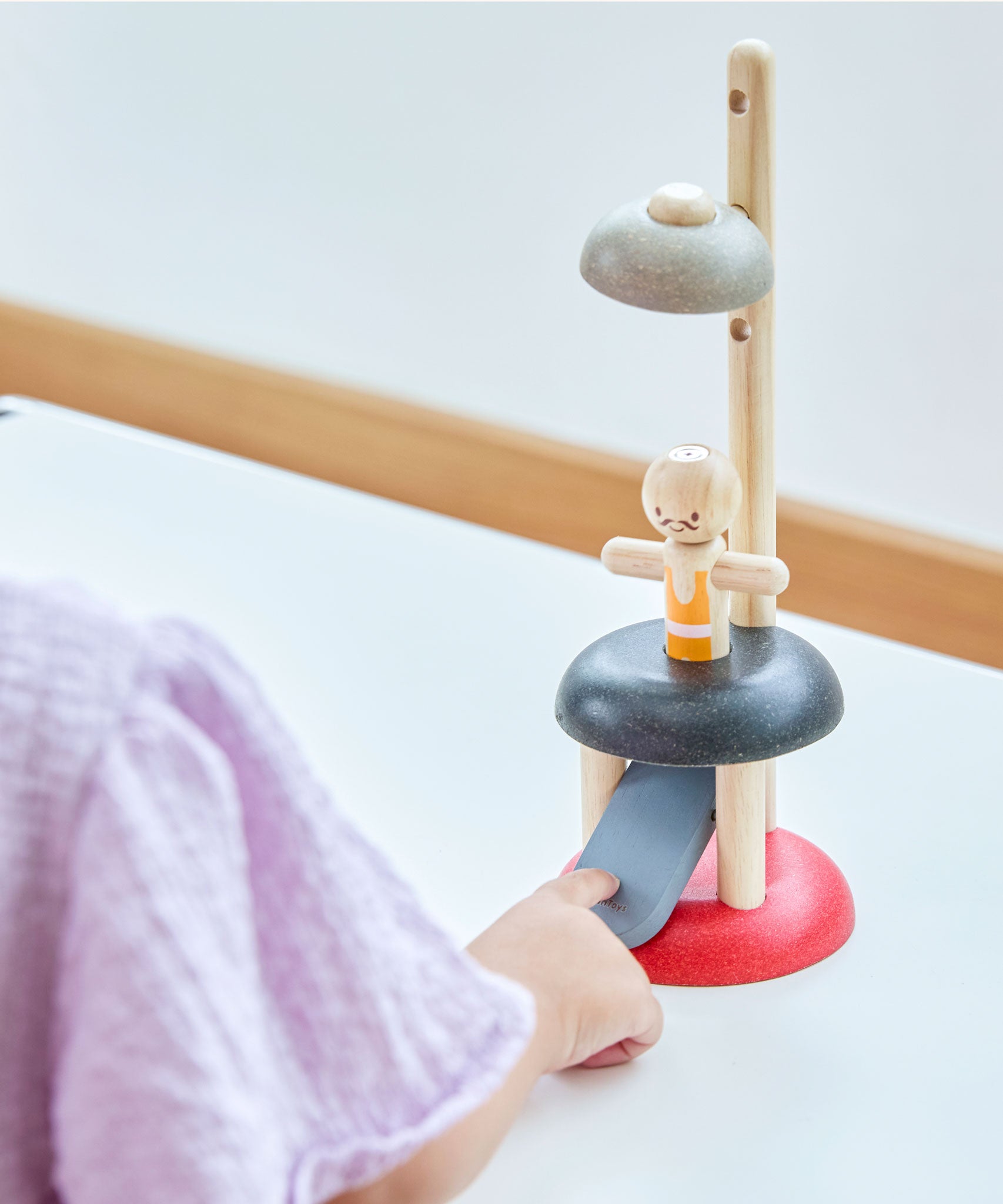 A child pressing the PlanToys Natural Rubberwood Jumping Acrobat Toy. PlanToys have a vast range of sustainable wooden toys are available at Babipur.