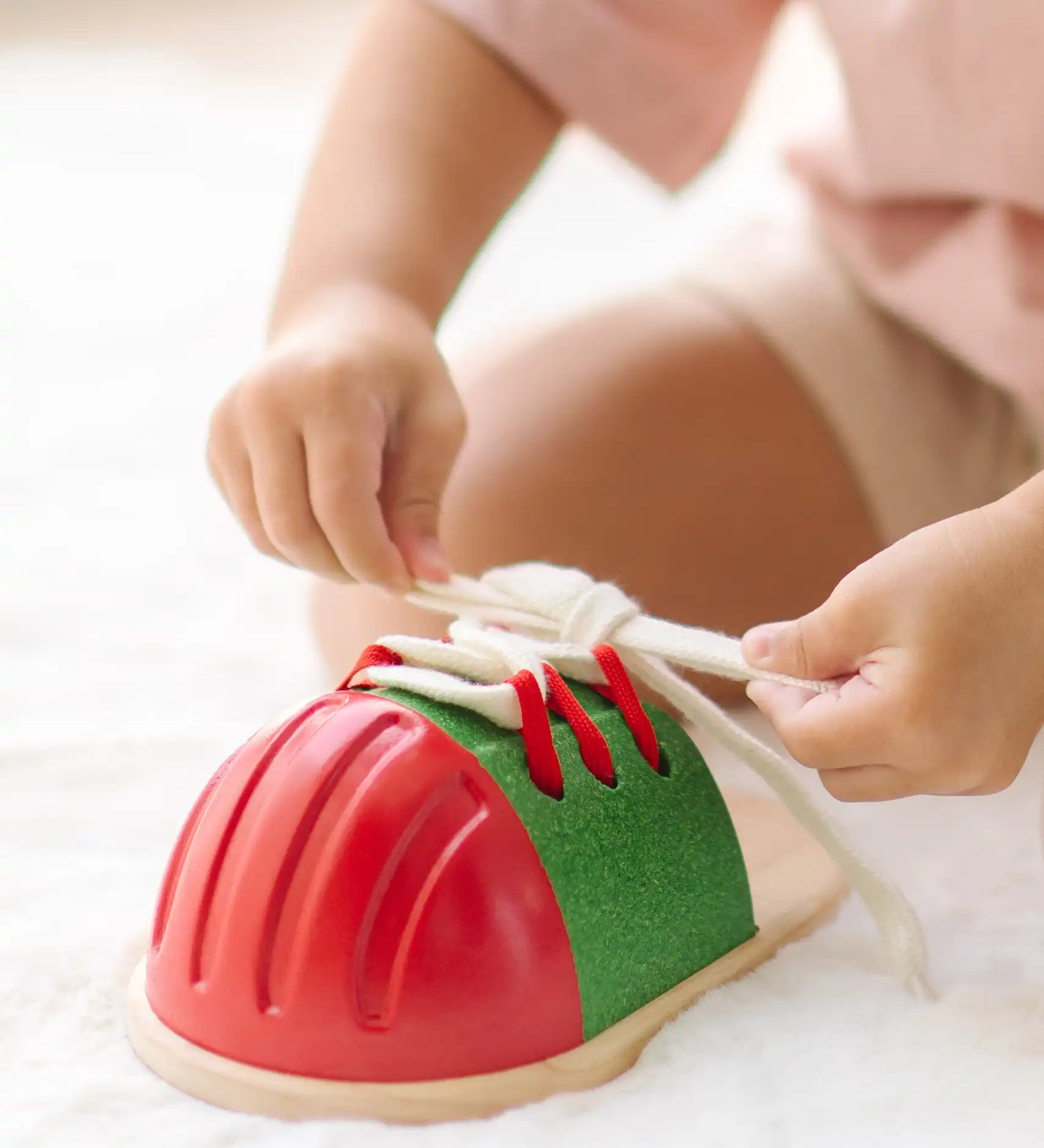 Child tying the laces on the PlanToys life size tie-up wooden shoe toy. 