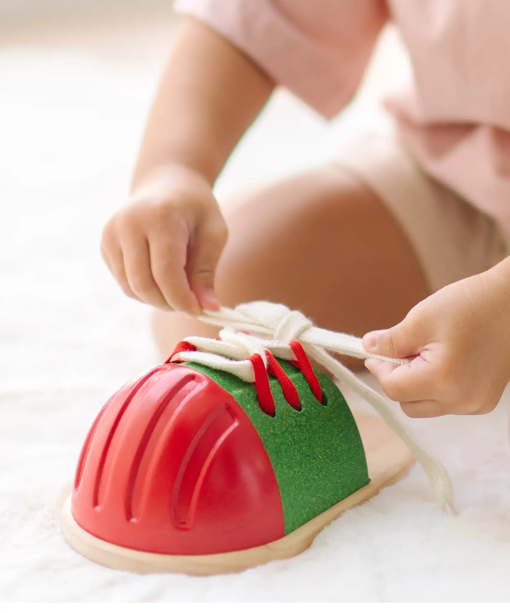 Child tying the laces on the PlanToys life size tie-up wooden shoe toy. 