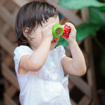 A child holding the green and red PlanToys Mushroom Kaleidoscope up to their eyes. 