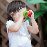 A child holding the green and red PlanToys Mushroom Kaleidoscope up to their eyes. 
