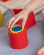 Close up of young child making a stack with the PlanToys matching and nesting shapes on a grey bed