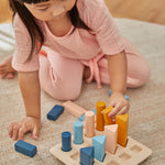 Young child crouched down placing shapes in the PlanToys wooden orchard peg board toy