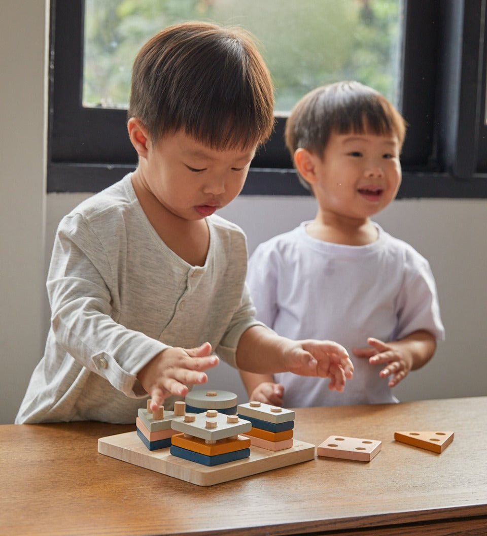Two boys playing with the PlanToys plastic-free wooden orchard shape sorting toy on a wooden table