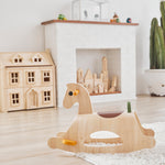 PlanToys childrens wooden Palomino rocking horse on a white fluffy rug in front of a fireplace and Victorian dollhouse