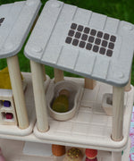 An overhead angle view of the PlanToys PlanSpace bathroom set attached to the other sets from the PlanSpace collection. The solar panel details on the roof can be seen and a green coloured Nin peg doll has been placed laying down in the bath. 