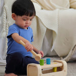 A child playing with the PlanToys Pounding Bench, and using the hammer/mallet to hammer the pegs through the holes.