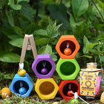 The Plan Toys Bee Hives Rainbow hives stacked up outdoors, some of the bees are in the matching coloured hives. There are Grapat honeycomb pieces placed in front of them and a pollinator seedbom by the side. 