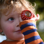 A child holding a red PlanToys Mushroom Kaleidoscope up to their eye. 