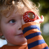A child holding a red PlanToys Mushroom Kaleidoscope up to their eye. 