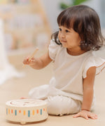 Child playing with the PlanToys wooden sensory drum musical toy with the wood drumstick in hand.