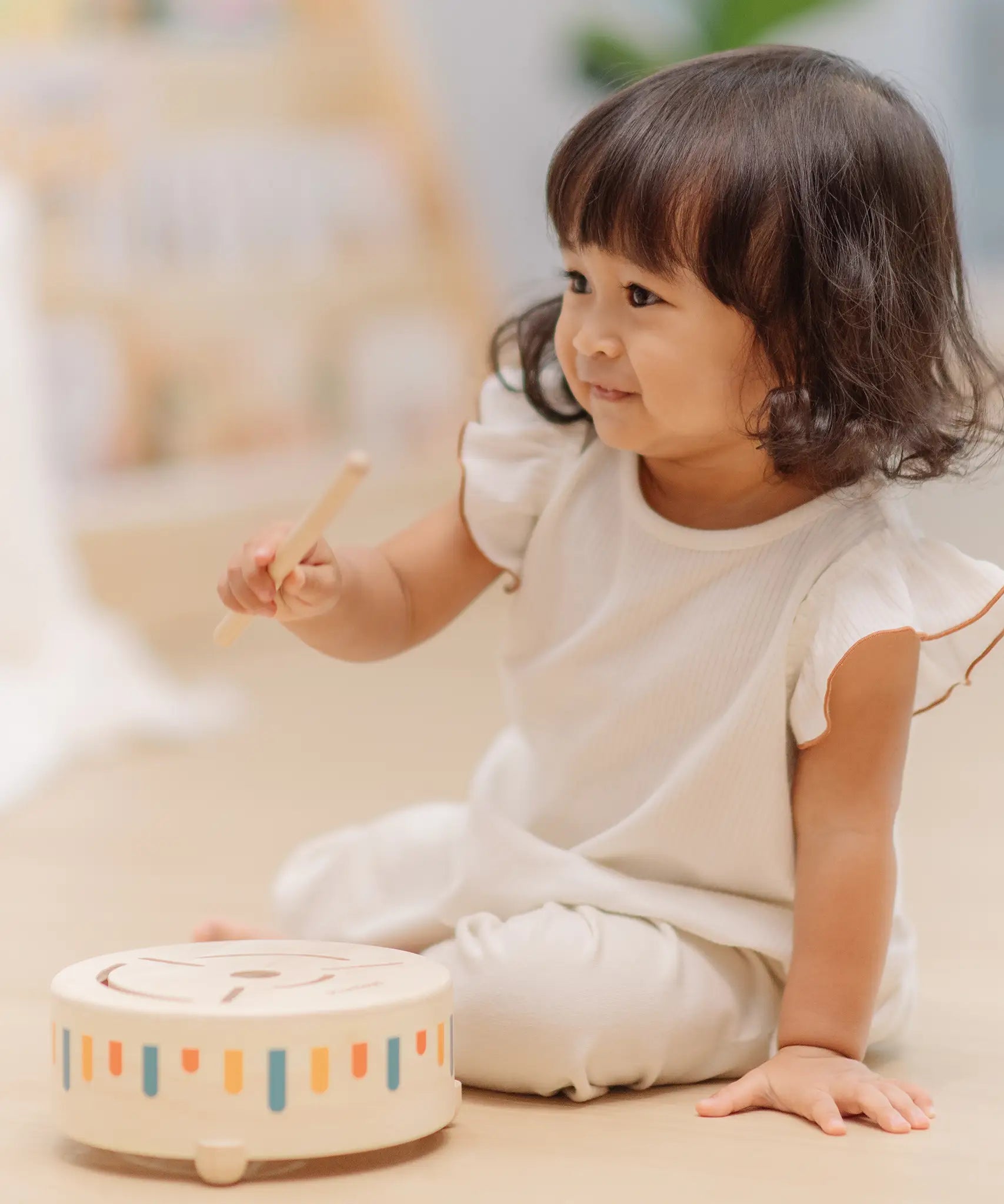 Child playing with the PlanToys wooden sensory drum musical toy with the wood drumstick in hand.