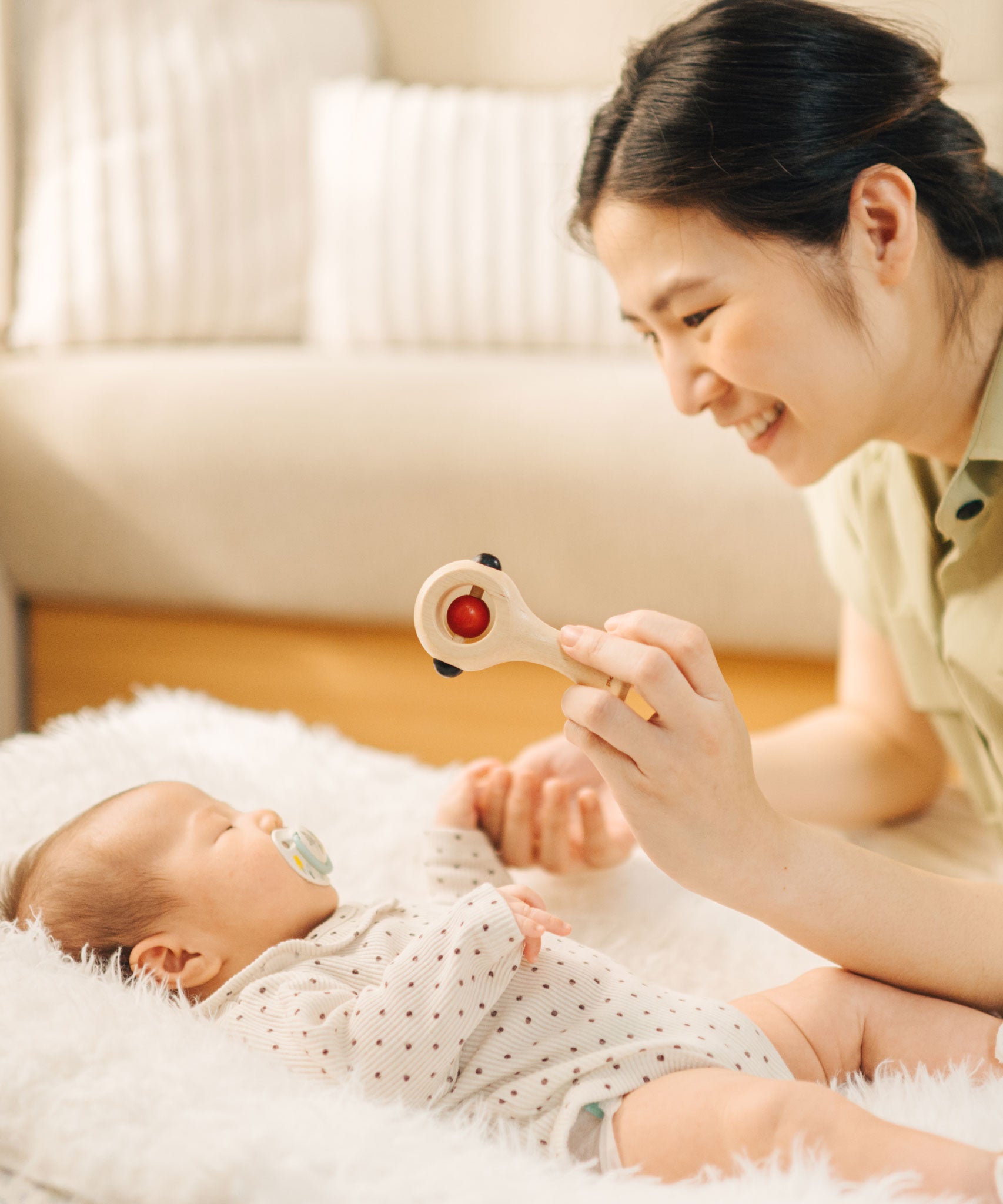 An adult holding up the PlanToys Shaking Rattle in a High Contrast colourway above a baby. The red and black details stand out against the natutral rubberwood body. PlanToys range of toys are made from sustainably sourced rubberwood, we're proud stockists of PlanToys here at Babipur. 