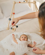 An adult holding the PlanToys high contrast square clutching toy above a baby that is laying underneath a baby gym. PlanToys range of toys are made from sustainably sourced rubberwood, we're proud stockists of PlanToys here at Babipur. 