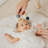 An adult holding the PlanToys high contrast square clutching toy above a baby. PlanToys range of toys are made from sustainably sourced rubberwood, we're proud stockists of PlanToys here at Babipur. 