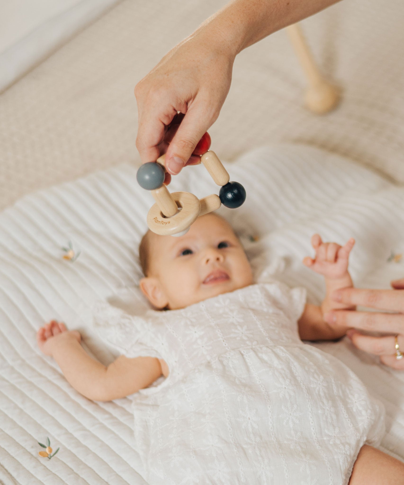 An adult holding the PlanToys high contrast square clutching toy above a baby. PlanToys range of toys are made from sustainably sourced rubberwood, we're proud stockists of PlanToys here at Babipur. 