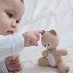 A baby playing with a PlanToys wooden toy bear on a white material. 