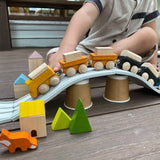 Child pulling the PlanToys yellow wooden cargo train across a rubber railway track placed over upturned cups.  