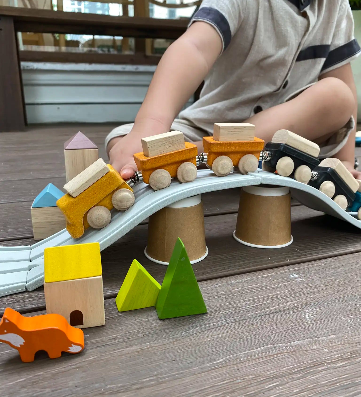 Child pulling the PlanToys yellow wooden cargo train across a rubber railway track placed over upturned cups.  