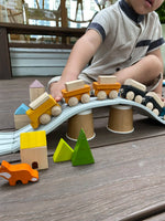 Child pulling the PlanToys yellow wooden cargo train across a rubber railway track placed over upturned cups.  