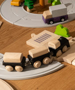PlanToys black wooden classic toy train placed on rubber train tracks and wooden roads.