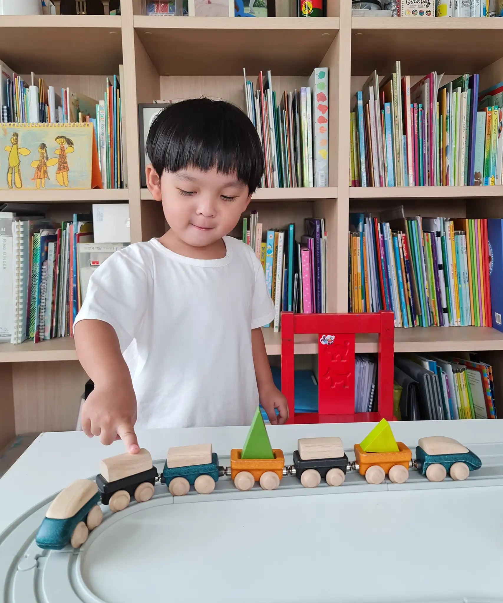 Child playing with PlanToys blue wooden trains on a rubber railway tracks. 