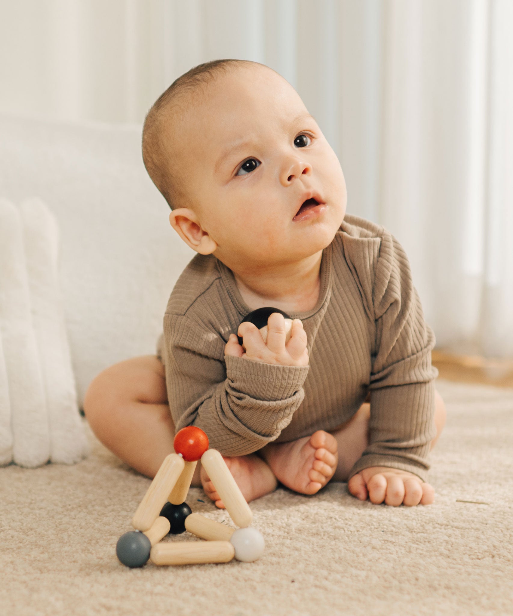 A baby holding the ball from the PlanToys high contrast Triangle baby Clutching Toy. A black and natural wood wooden ball in a stretchy triangle clutching toy. PlanToys range of toys are made from sustainably sourced rubberwood, we're proud stockists of PlanToys here at Babipur. 
