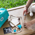 A close up of a child's hand playing with the Plan Toys Play Vet Set. 