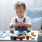 Child sat at a table threading plastic-free lacing blocks onto a blue string