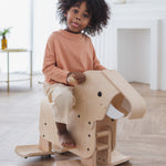 A child riding on a PlanToys Walking Elephant, they have a playful expression and are sticking their tongue out. 