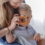 A child with an adult playing with the PlanToys Yellow My First Camera in Orchard colour way.