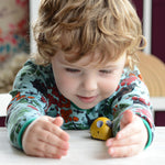 A child playing with a yellow PlanToys Wooden Pull-Back Mouse.