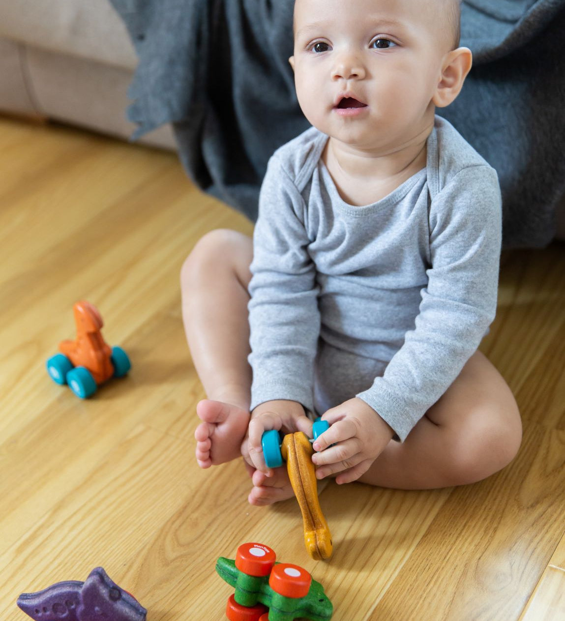 Toddler playing with four PlanToys Dino Cars on a wooden floor