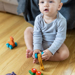 Child playing with four PlanToys Dino Cars on a wooden floor.
