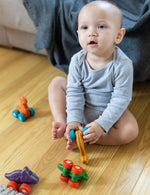 Child playing with four PlanToys Dino Cars on a wooden floor.