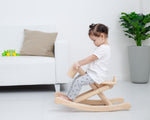 A child is rocking on the PlanToys Foldable Rocking Horse in a living room setting. 