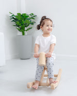 Toddler sat on the wooden foldable rocking horse by PlanToys. Side view.