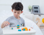 A child playing with the PlanToys mini stacking game on a small table.