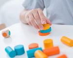 A close up of a child's hands playing with the PlanToys mini stacking game on a small table.
