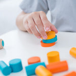 A close up of a child's hands playing with the PlanToys mini stacking game on a small table.